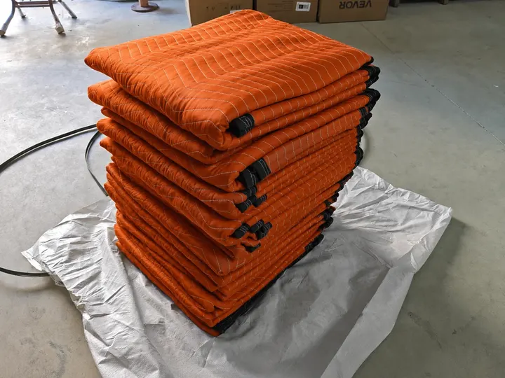 Stack of folded orange polyester moving pads with black trim on a warehouse floor